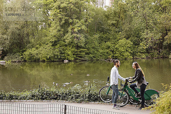 Hochwinkelansicht eines glücklichen Paares  das sich im Stehen mit Fahrrädern am See unterhält