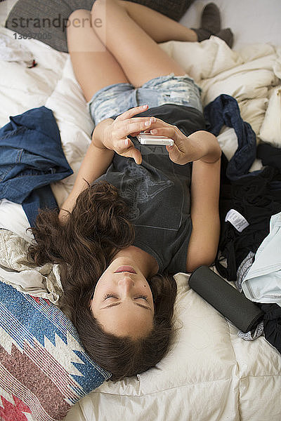 Hochwinkelansicht einer Frau  die ein Smartphone benutzt  während sie zu Hause im Bett liegt