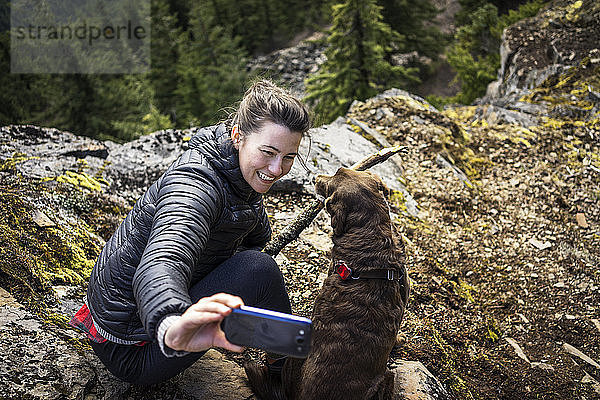 Hochwinkelaufnahme einer Frau  die mit ihrem Hund auf einem Bergfelsen klickt