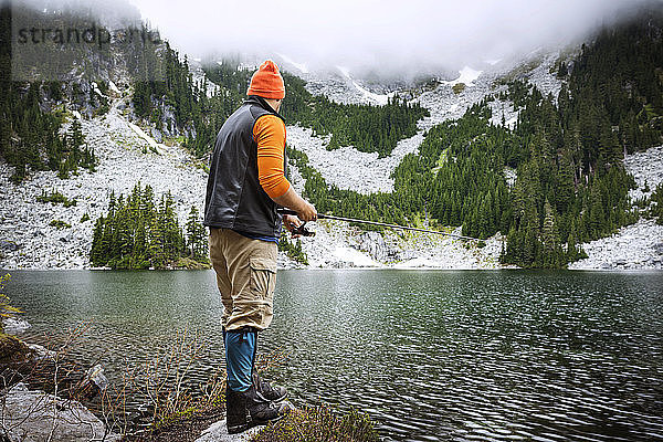Rückansicht eines Mannes  der am See gegen Berge fischt