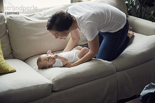 Schrägansicht einer glücklichen Mutter  die ihren Sohn zu Hause auf dem Sofa liegen sieht