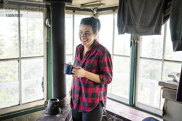 Glückliche Frau genießt Drink im Stehen in der Hütte