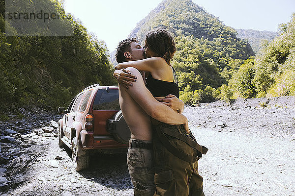 Seitenansicht eines Paares  das sich beim Küssen gegen Berge umarmt