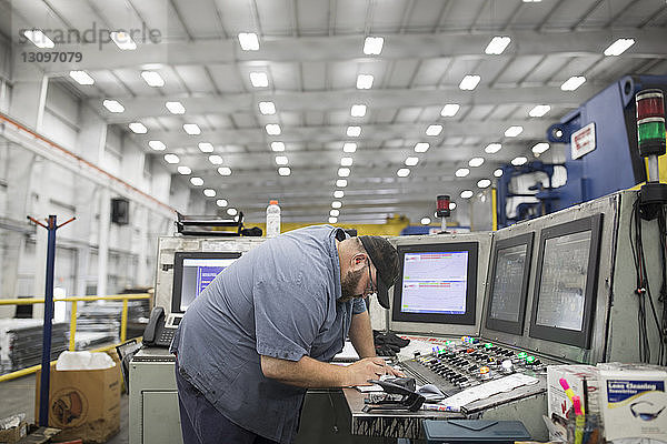 Seitenansicht eines Arbeiters  der eine Maschine in einer Fabrik der Stahlindustrie benutzt