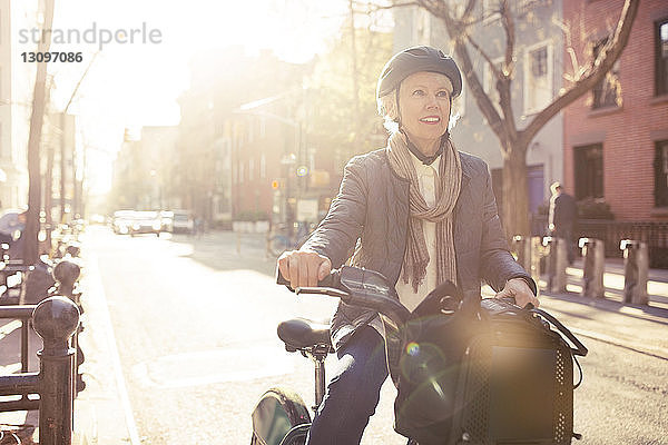 Lächelnde ältere Frau sitzt auf dem Fahrrad auf der Straße