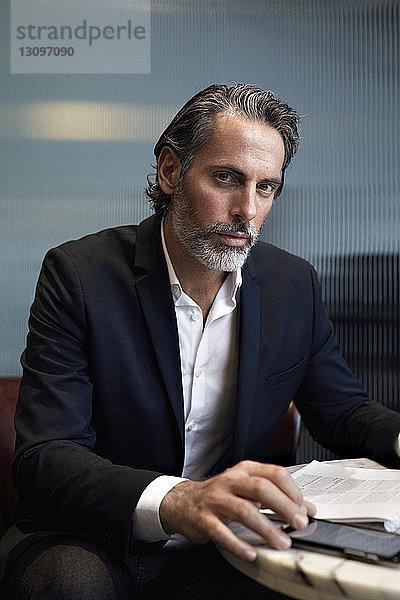 Porträt eines selbstbewussten Geschäftsmannes  der ein Smartphone benutzt  während er im Büro sitzt