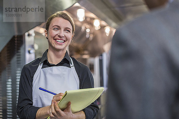 Lächelnde Küchenchefin mit Notizblock im Gespräch mit Restaurantbesitzer in der Küche