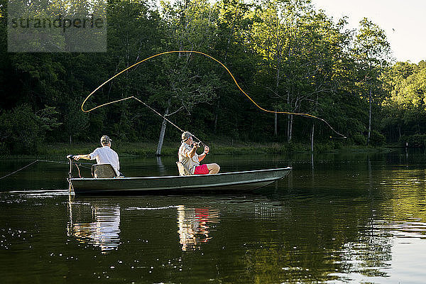 Mann wirft Angelschnur im See aus  Freund sitzt im Ruderboot