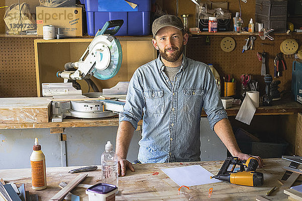 Porträt eines selbstbewussten Künstlers  der im Workshop an der Werkbank steht