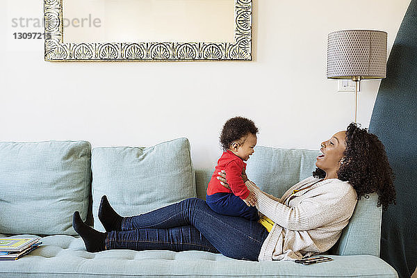 Glückliche Frau spielt mit ihrem Sohn  während sie zu Hause auf dem Sofa sitzt