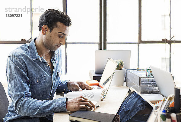 Selbstbewusster Geschäftsmann liest Buch am Schreibtisch im Büro