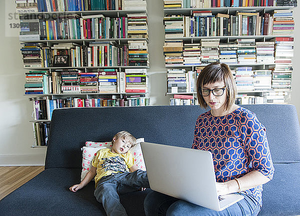 Mutter benutzt Laptop-Computer  während sie mit ihrem Sohn zu Hause auf dem Sofa sitzt