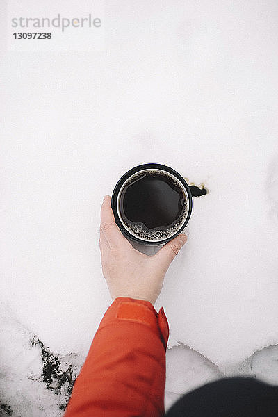 Abgehackte Hand einer Frau  die schwarzen Kaffee in einer Tasse auf Schnee hält