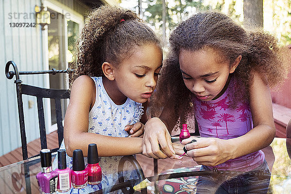 Mädchen trägt Nagellack auf die Fingernägel der Schwester auf  während sie im Hof am Tisch sitzt