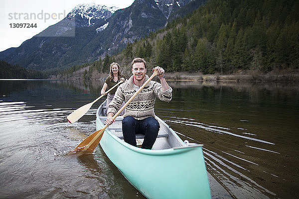 Glückliches junges Paar beim Kanufahren auf See gegen Berge
