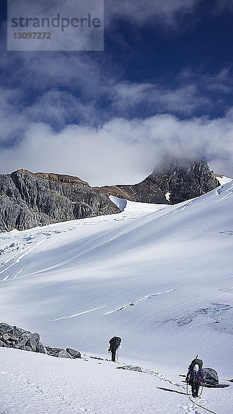 Männer wandern auf schneebedecktem Berg gegen den Himmel