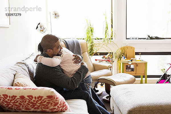 Seitenansicht eines Mannes  der seine Tochter umarmt  während er auf dem Sofa sitzt