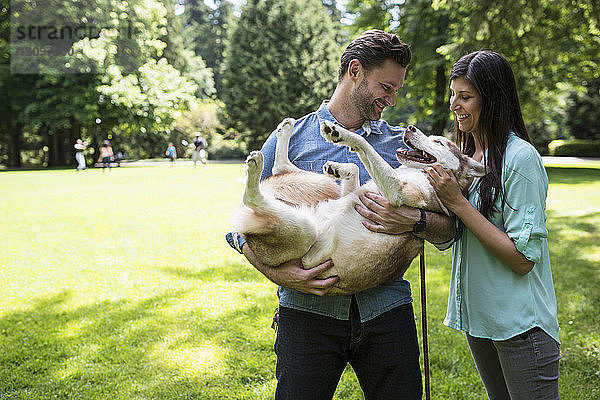 Glückliches Paar spielt mit Hund im Park