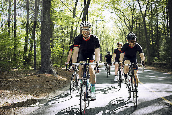 Lächelnder männlicher Radfahrer fährt mit Freunden auf der Landstraße Fahrrad