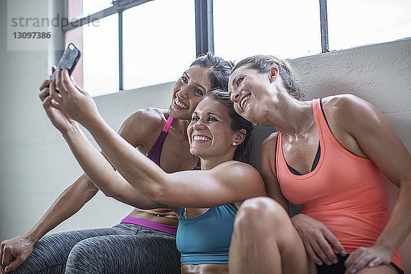 Glückliche Freundinnen  die sich im Fitnessclub über das Mobiltelefon selbstständig machen