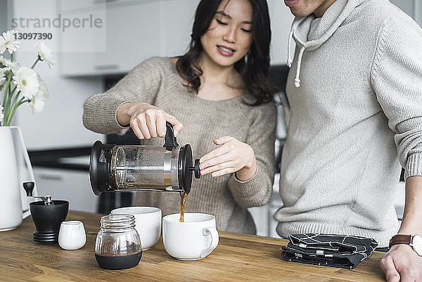 Frau mit Freund gießt bei Tisch Kaffee in Tassen