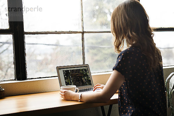 Rückansicht einer Frau mit Laptop auf einem Tisch im Café