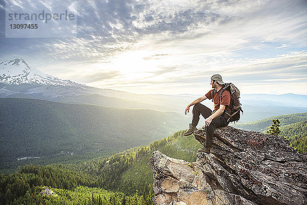 Wanderer schaut weg  während er auf einem Berg vor bewölktem Himmel sitzt