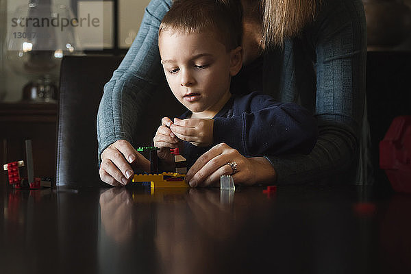 Mittelteil der Mutter  die dem Sohn bei der Herstellung von Spielzeugblöcken am Tisch hilft