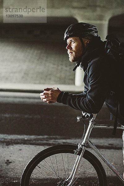 Männlicher Pendler mit Fahrrad  der auf der Brücke stehend wegschaut