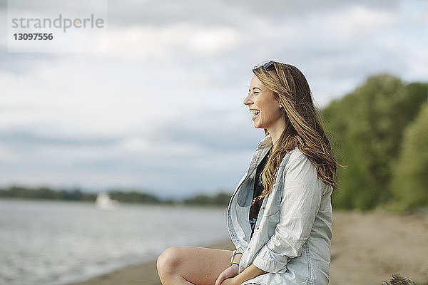Seitenansicht einer glücklichen Frau am Flussufer sitzend