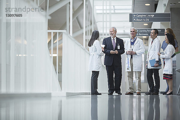 Leitender Arzt diskutiert mit Kollegen  während er im Krankenhauskorridor steht