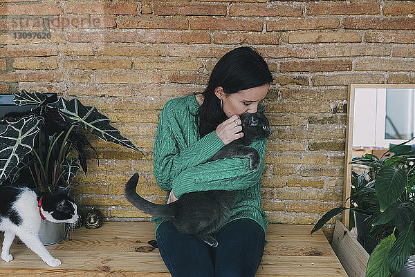 Frau küsst Katze  während sie zu Hause an einer Ziegelmauer sitzt