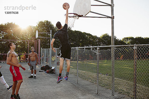 Freunde sehen Mann beim Dunking beim Basketballspielen auf dem Platz