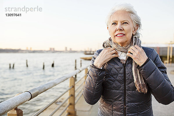 Nachdenkliche ältere Frau mit Schalldämpfer auf der Promenade bei Sonnenuntergang