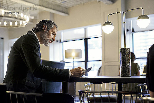 Geschäftsmann studiert Dokumente  während er im kreativen Büro mit einer Kollegin im Hintergrund sitzt