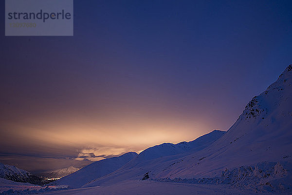 Szenische Ansicht eines schneebedeckten Berges vor bewölktem Himmel bei Sonnenuntergang
