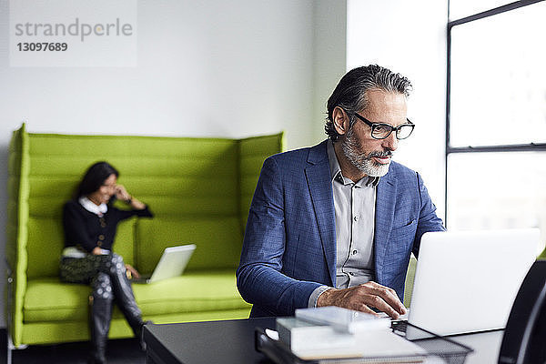 Geschäftsmann benutzt Laptop-Computer mit einer im Hintergrund arbeitenden Kollegin