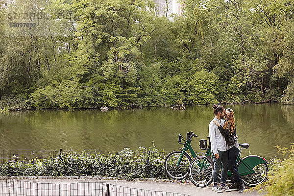Glücklicher Mann küsst im Stehen mit Fahrrädern am See seine Freundin