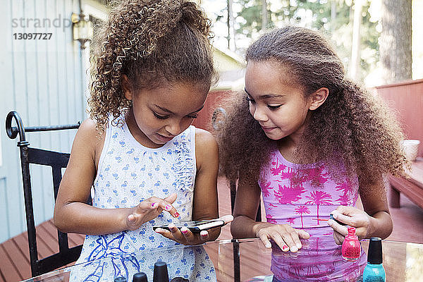 Mädchen benutzen ein Smartphone  während sie im Hof am Tisch sitzen