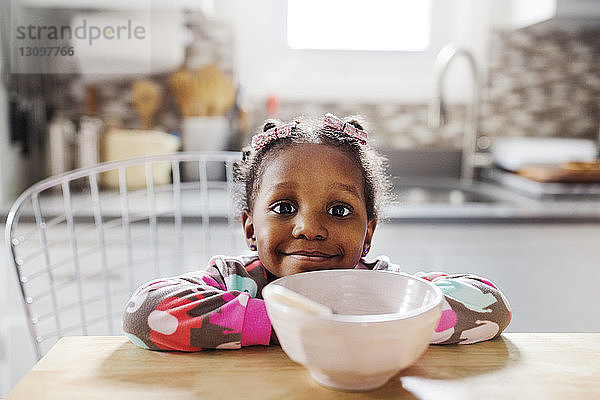 Porträt eines niedlichen Mädchens  das sich auf einen Tisch lehnt  mit einer Frühstücksschüssel im Vordergrund