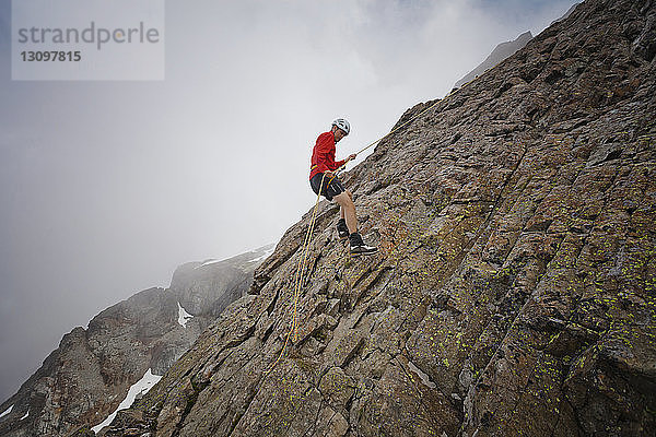 Seitenansicht eines Wanderers mit Seil beim Klettern an Felsformationen gegen Wolken