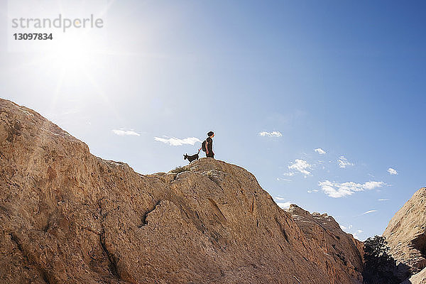 Tiefwinkelaufnahme eines Mannes mit Hund  der auf einem Berg vor blauem Himmel steht