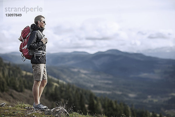 Wanderer trägt Rucksack  während er auf Berg gegen Himmel steht