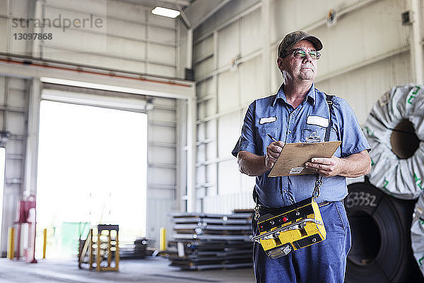 Arbeiter hält Klemmbrett in der Hand  während er in einer Fabrik der Metall-Stahlindustrie arbeitet