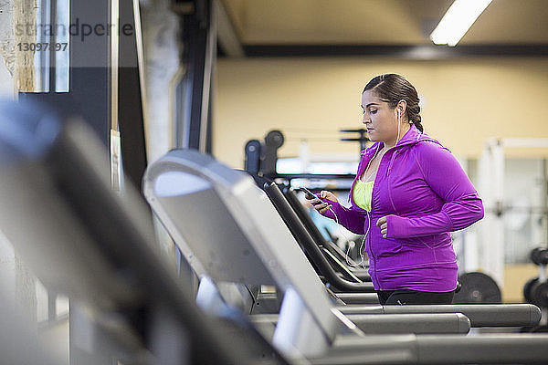 Frau benutzt Mobiltelefon beim Training auf dem Laufband im Fitnessstudio