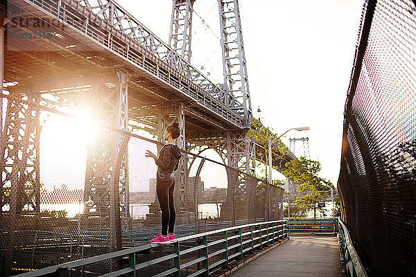 Frau steht auf einem Geländer und schaut an einem sonnigen Tag auf die Williamsburg Bridge