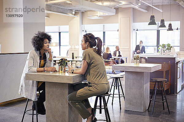 Geschäftsfrauen im Gespräch in der Cafeteria im Kreativbüro mit Kollegen im Hintergrund