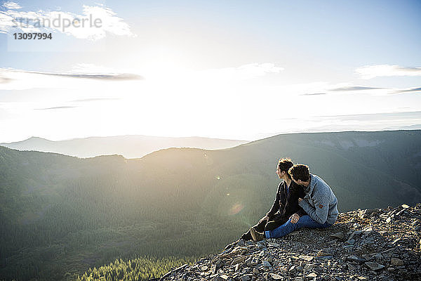 Ehepaar sitzt auf einem Bergfelsen und schaut sich die Aussicht an