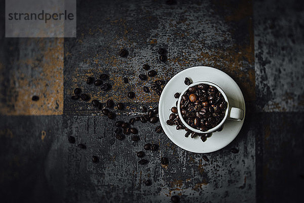 Draufsicht auf Kaffeebohnen in Tasse mit Untertasse auf altem Tisch