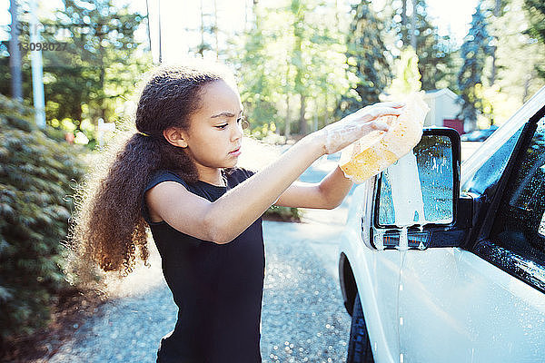 Mädchen wäscht Auto  während sie an der Einfahrt steht